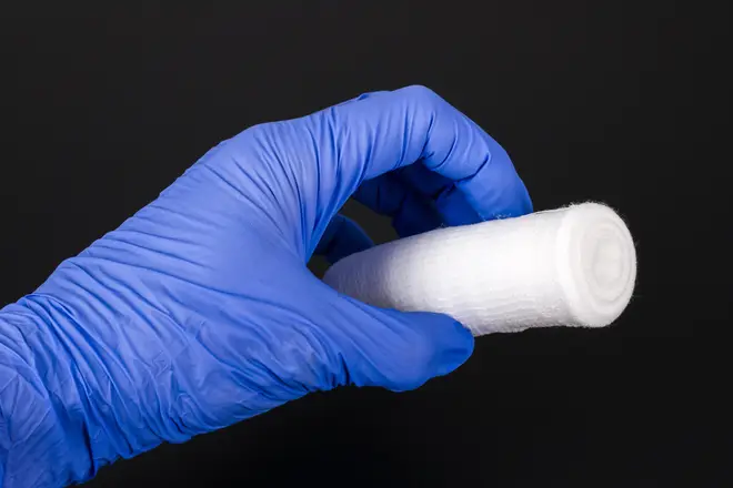 A hand in a blue medical glove is holding a white gauze