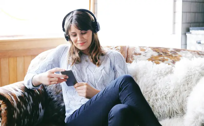 Stock photo of a woman looking at her phone wearing headphones