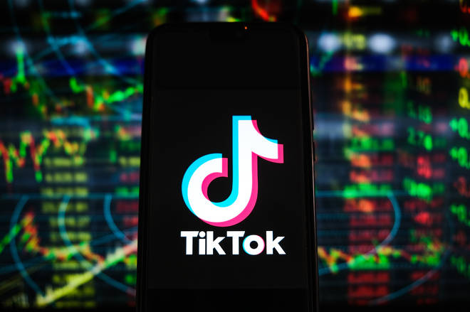 A TikTok logo is displayed on a smartphone with stock market percentages in the background.