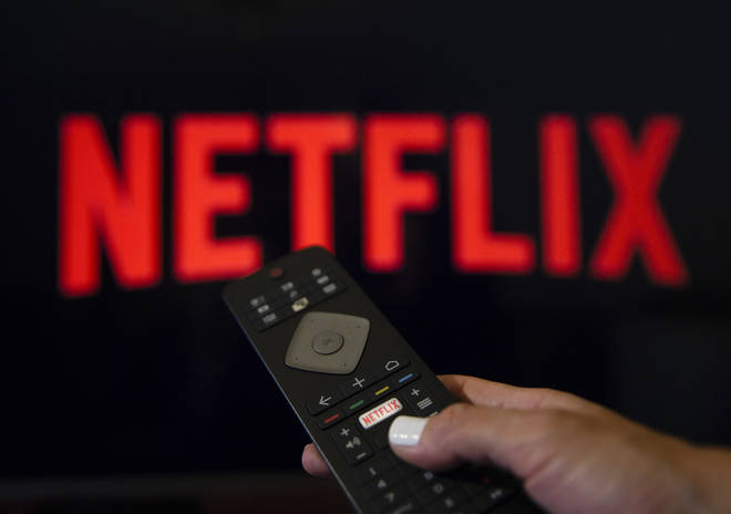 A person holds a Netflix remote control in front of the logo of Netflix application